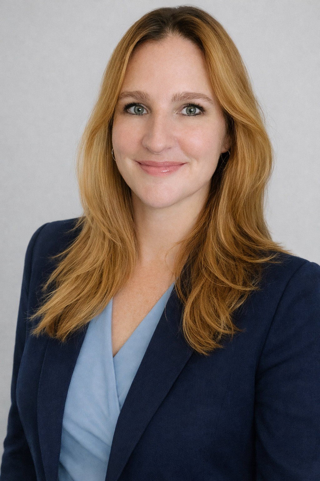 Professional headshot of a female attorney with long, wavy blonde hair, wearing a navy blazer over a light blue top, conveying a sense of approachability and expertise in family law.