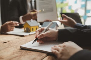 Hands of professionals discussing asset valuation during a divorce, with a small house model and legal documents on the table.