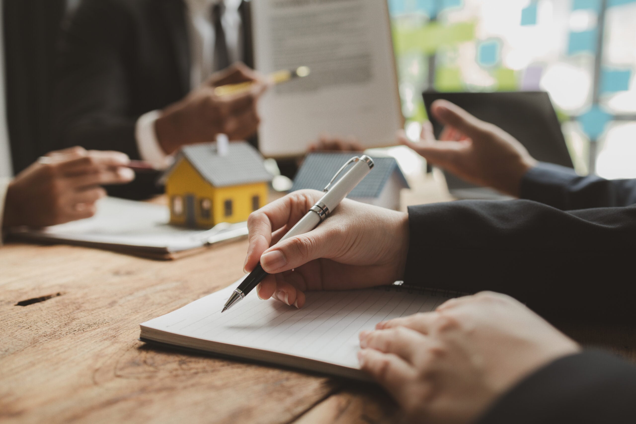 Hands of legal professionals reviewing property valuation documents, with a small model house on the table, emphasizing asset assessment in divorce proceedings.
