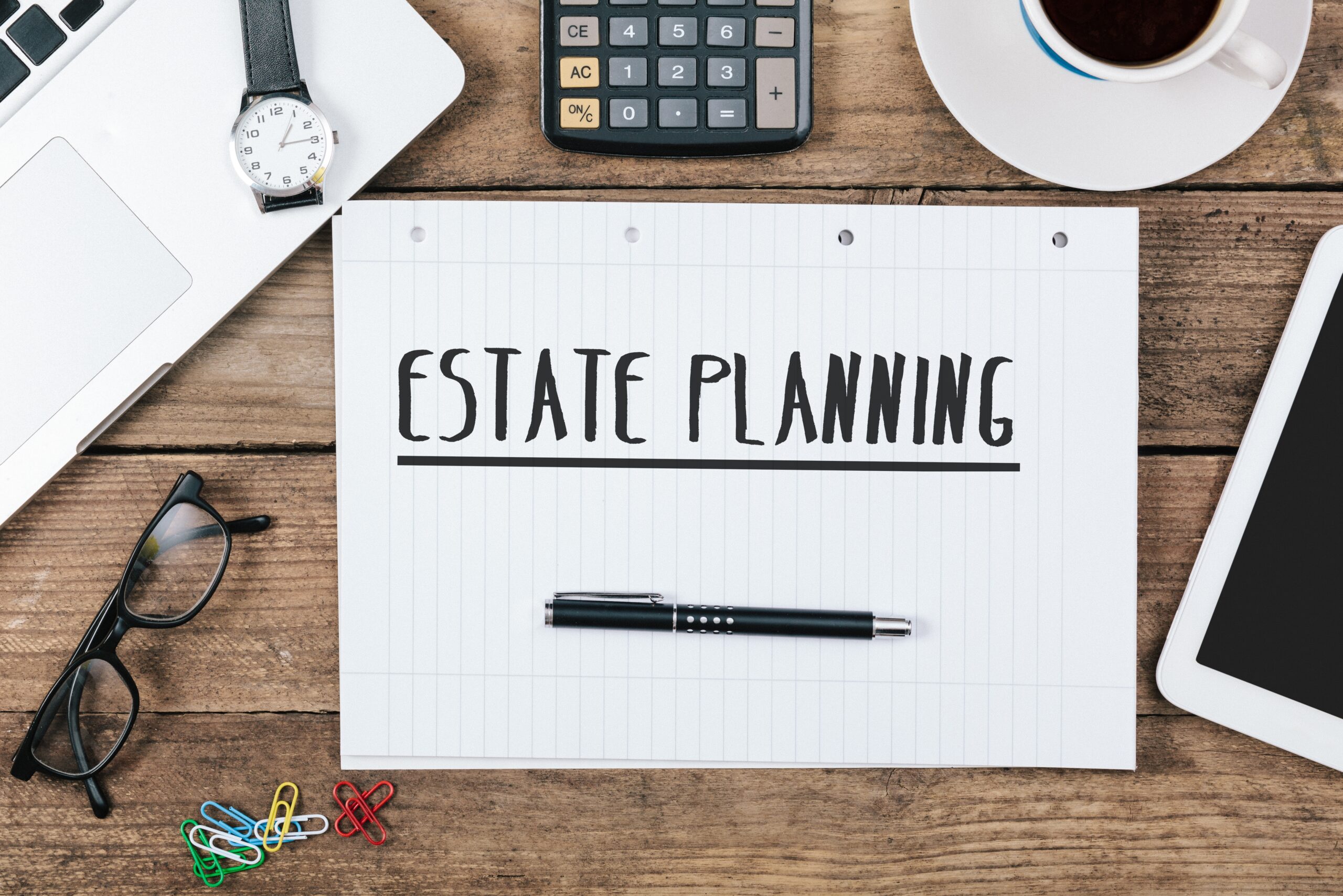 Estate planning concept with handwritten text on paper, surrounded by a laptop, calculator, glasses, pen, paper clips, and a coffee cup, symbolizing legal services in estate planning for families in Northwest Indiana and Chicagoland area.