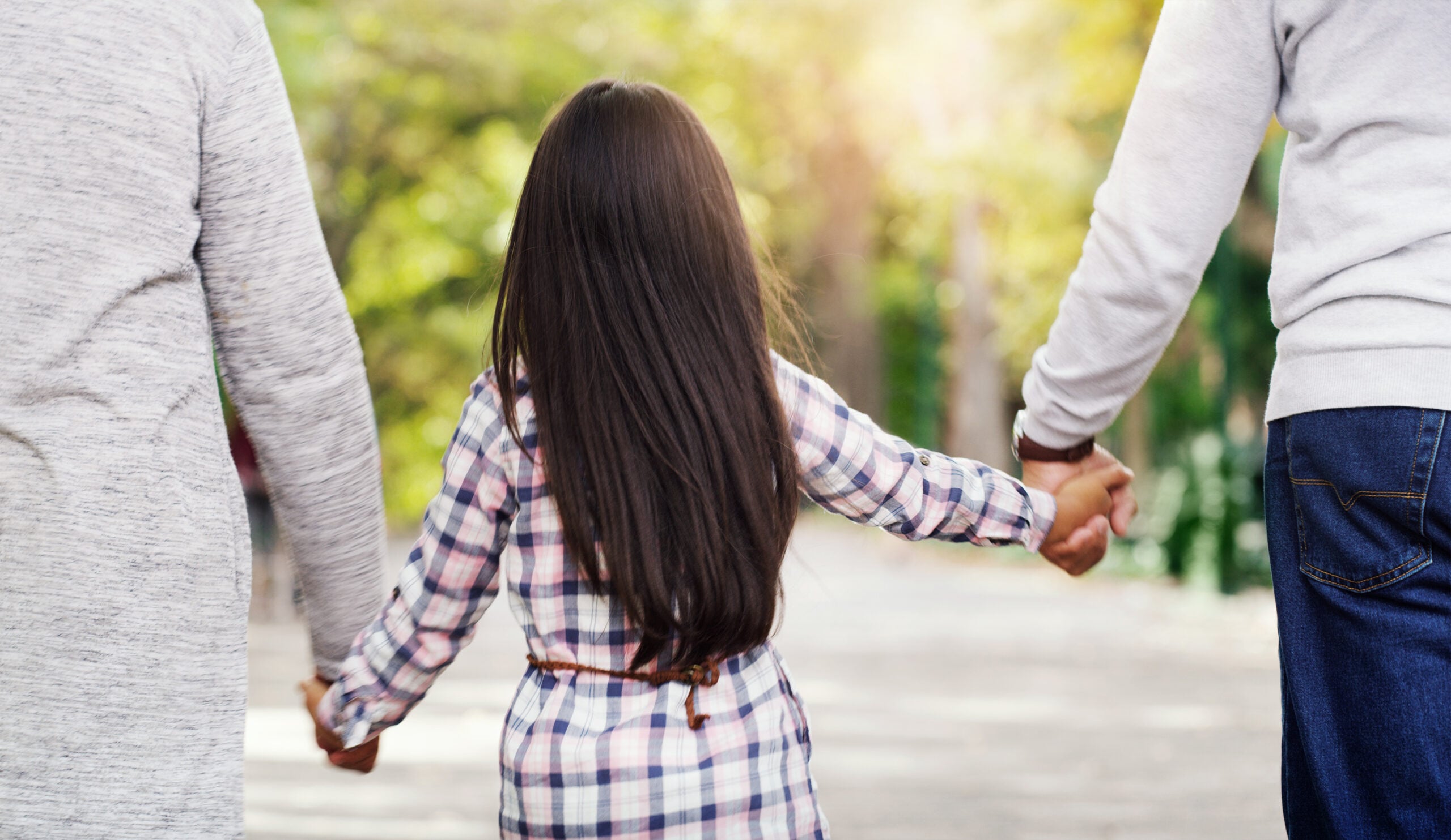 Child holding hands with two adults in a park, symbolizing family unity and support in child custody matters.