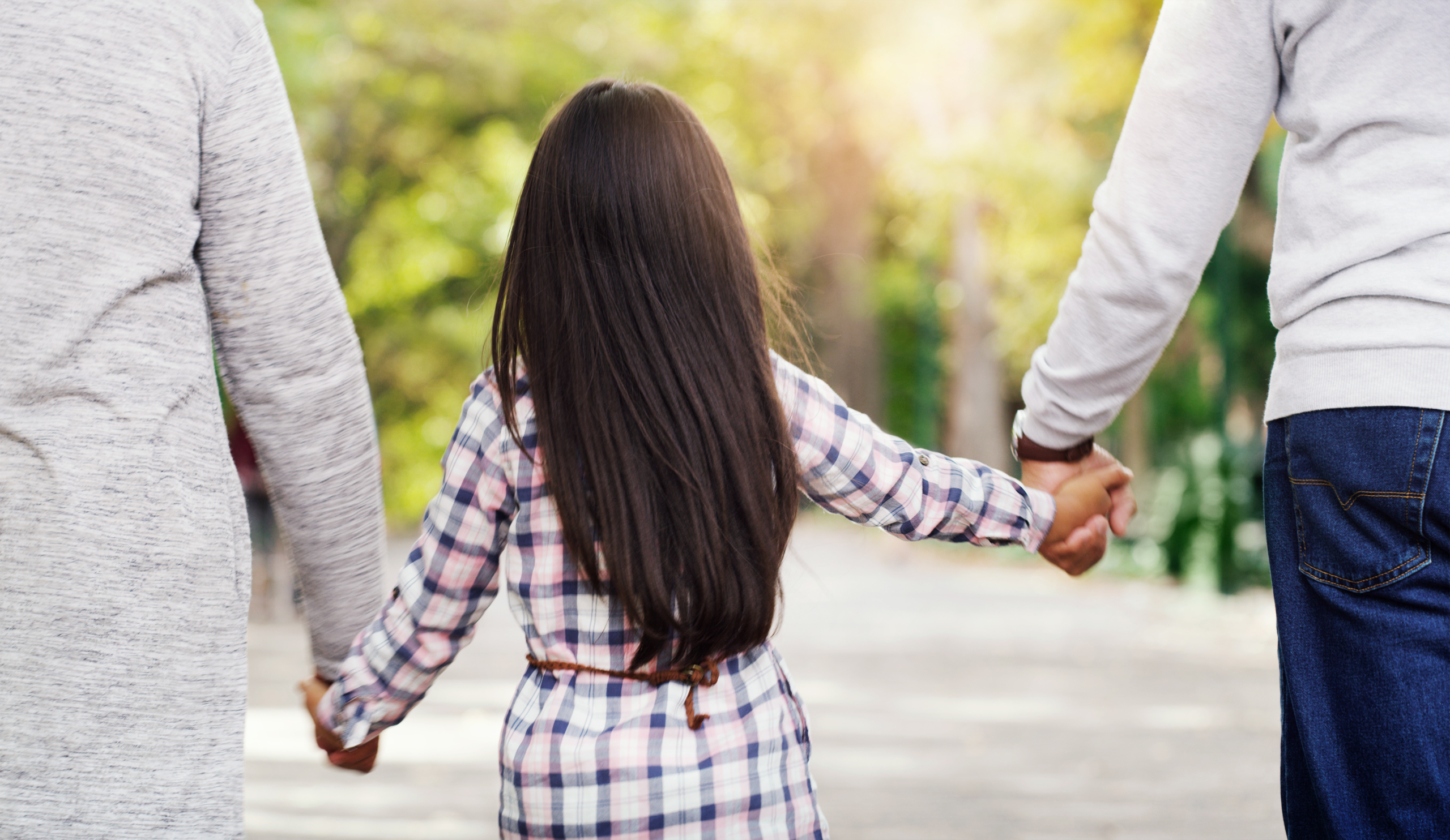 Parents holding hands with a child walking together, symbolizing family unity and support in child custody and child support matters.